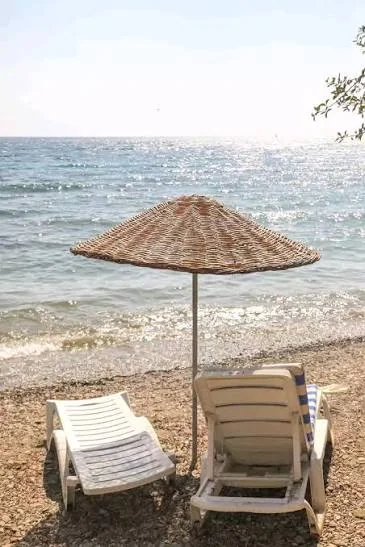 Pruva Pansiyon’un Mazı’daki çakıllı özel plajında hasır şemsiye ve şezlonglar