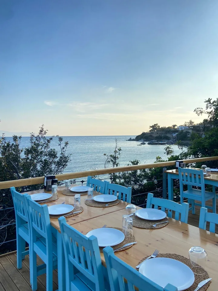 Pruva restoran terasında mavi sandalyeli masalar ve Mazı koyu manzarası